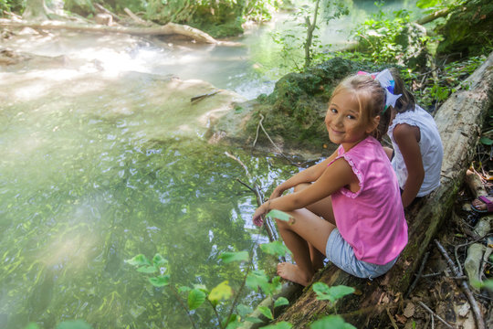 Two little girls relax at clean forest creek on summer day in nature