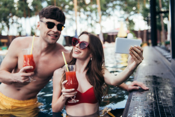 cheerful young woman taking selfie with boyfriend while relaxing in swimming pool together