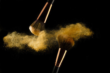 Cosmetic brush with golden powder spreading on black background