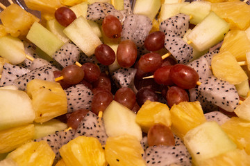 Barbecue style different types of fruit on stick beautifully arranged on a plate.