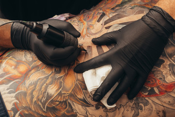 Close up tattoo machine. Tattooing. Man creating picture on his back by a professional tattoo artist. - obrazy, fototapety, plakaty