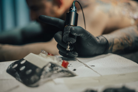 Close up tattoo machine. Tattooing. Man creating picture on his back by a professional tattoo artist.