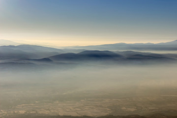 Soft, colorful, misty mountain layers and fields covered by golden fog during sunset
