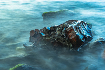Old rusty engine lying among stones in the water.