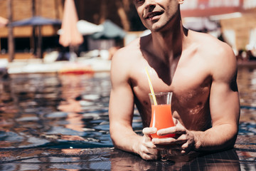 cropped view of handsome young man relaxing on poolside with glass of refreshing drink