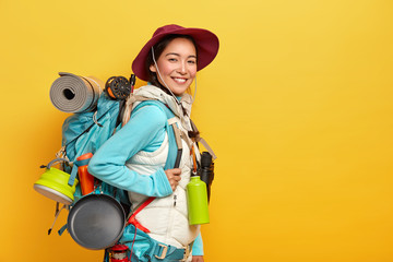 Happy brunette Asian traveler carries big tourist backpack, uses binoculars for journey, stands...