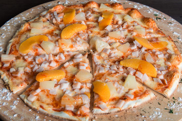 havaian pizza with ham and pineapples on a wooden plate