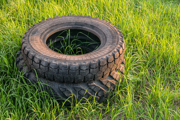 Car rubber tires thrown into a stack on green grass. Environmental pollution.