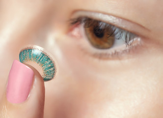 One woman holds a blue contact lens on her finger. Eye care and the choice between the means to...