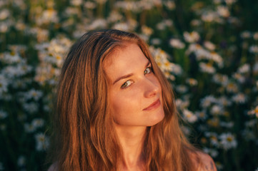Portrait of pretty blond woman sitting in chamomile field