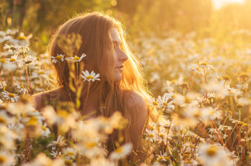 Side portrait of pretty blond woman sitting in chamomile field