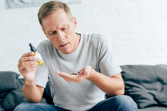 handsome man in t-shirt holding pills and cannabis oil