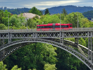 Red urban articulated bus crossing a metal bridge in the Swiss city of Bern