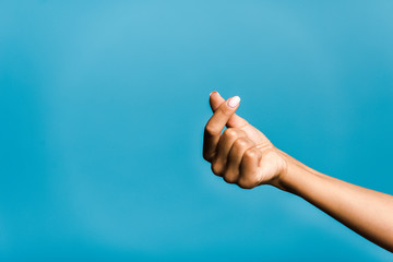 cropped view of young woman showing heart with hand isolated on blue