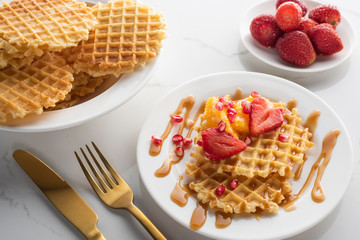 waffles with strawberries on a white plate on a white background with golden fork and knife