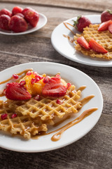waffles with strawberries on a white plate on a wooden background