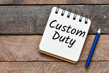 Custom duty text written in notebook on wooden background, top view
