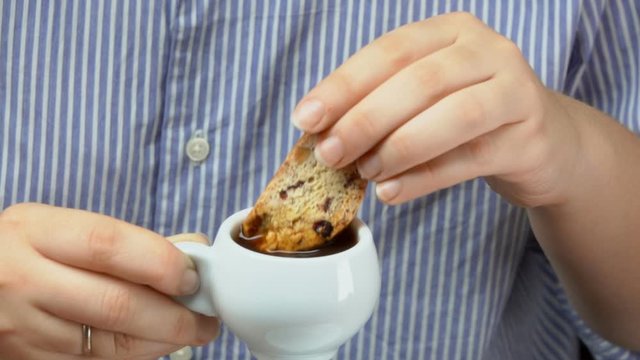 Woman dips cantucci cookies from a glass jar into an espresso coffee