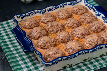 Process of cooking meatballs with rice, which are prepared in ceramic form and poured with sauce, against a dark background, horizontal orientation