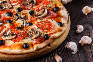 Pizza with tomato, olives, champignons, ham and cheese on round wooden plate