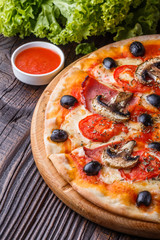 Pizza with tomato, olives, champignons, ham and cheese on round wooden plate