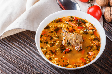 Georgian soup. Kharcho with rice, tomato, beef, garlic and herbs in bowl on wooden table