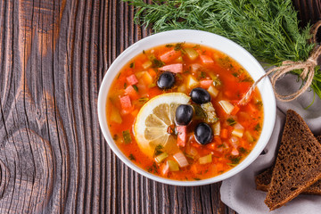 Traditional Russian meat soup Solyanka in bowl on rustic wooden table