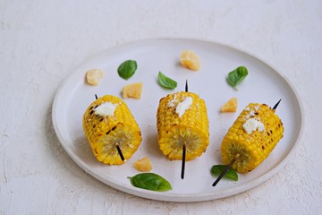 Grilled corn skewers on a white ceramic tray. Served with salted butter and grated Parmesan cheese. Vegetable dishes. Harvest the corn.