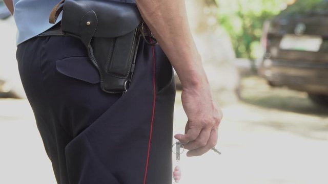 a policeman with a holster, a gun on his belt, holds keys with a keychain in his hand, on guard of the law, protection of legitimate interests, public safety
