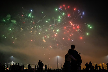 silhouettes of people watching fireworks in the background of bright flashes in the night sky