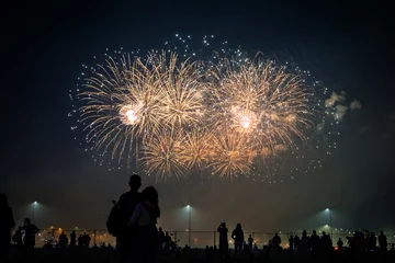 Silhouetten von Menschen, die ein Feuerwerk im Hintergrund heller Blitze am Nachthimmel beobachten © Sergey