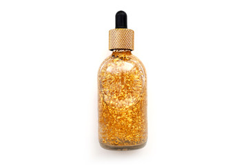 Anti-aging serum with gold particles in a transparent glass bottle on a white background.