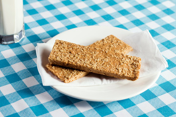 Vanilla energy bar served on white plate with a glass of milk on a table with light blue checkered tablecloth
