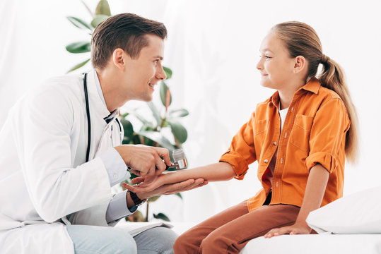 smiling pediatrist in white coat examining child with dermascope