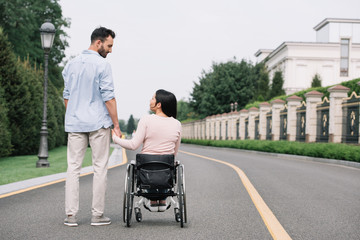 back view of young man and disabled woman holding hands while walking in park