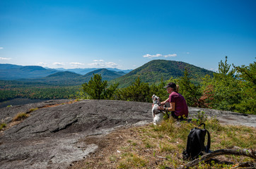 Fototapeta na wymiar Woman and dog enjoying the view of Adirondack mountain range from the summit of Clark Mountain