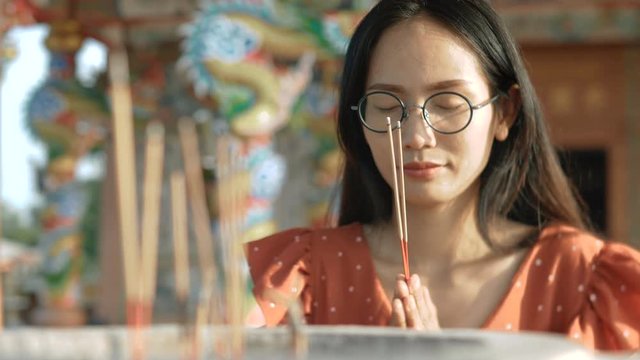 Young Asian woman in a buddhist temple puts an aromatic stick censer