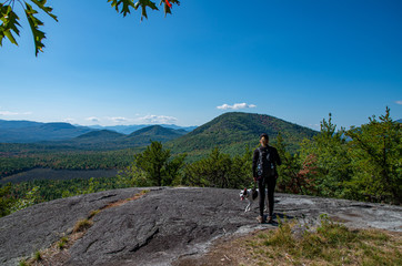 Fototapeta premium Woman and dog enjoying the view of Adirondack mountain range from the summit of Clark Mountain