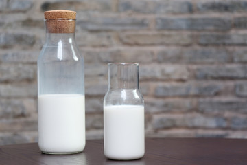 Glass of milk and half bottle of milk on table with blur wall background.