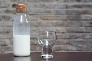 Empty glass and half bottle of milk on table with blur wall background.