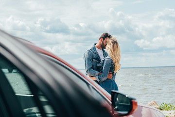 selective focus of woman and man in denim jackets kissing outside