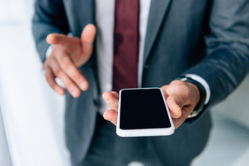 selective focus of businessman in formal wear holding smartphone with blank screen