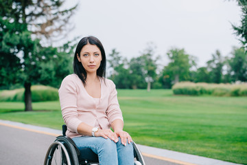 pensive disabled woman looking at camera while sitting in wheelchair in park