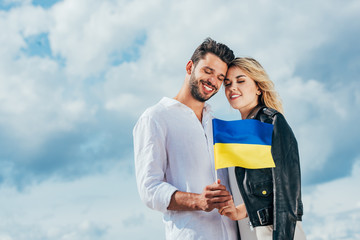 attractive woman and handsome man holding ukrainian flag outside