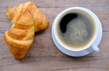 cup of coffee and croissant on wooden table