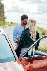 blonde woman and handsome man kissing and hugging near car