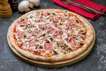 Pizza with ham and mushrooms on grey concrete table