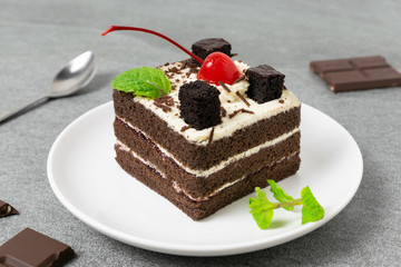 Yummy chocolate cake with cherry and mint leaves in white dish on tile table.