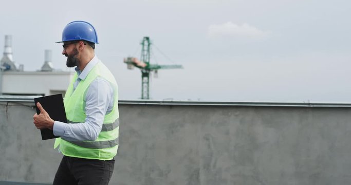 On the rooftop of construction site happy excited dancing engineer or architect moving happy in front of the camera and feeling great wearing a safety helmet and ration with a tablet
