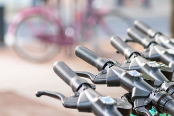 Lenker von E-Scootern im Vordergrund mit Fahrrad im unscharfen Hintergrund als Gegensatz und...